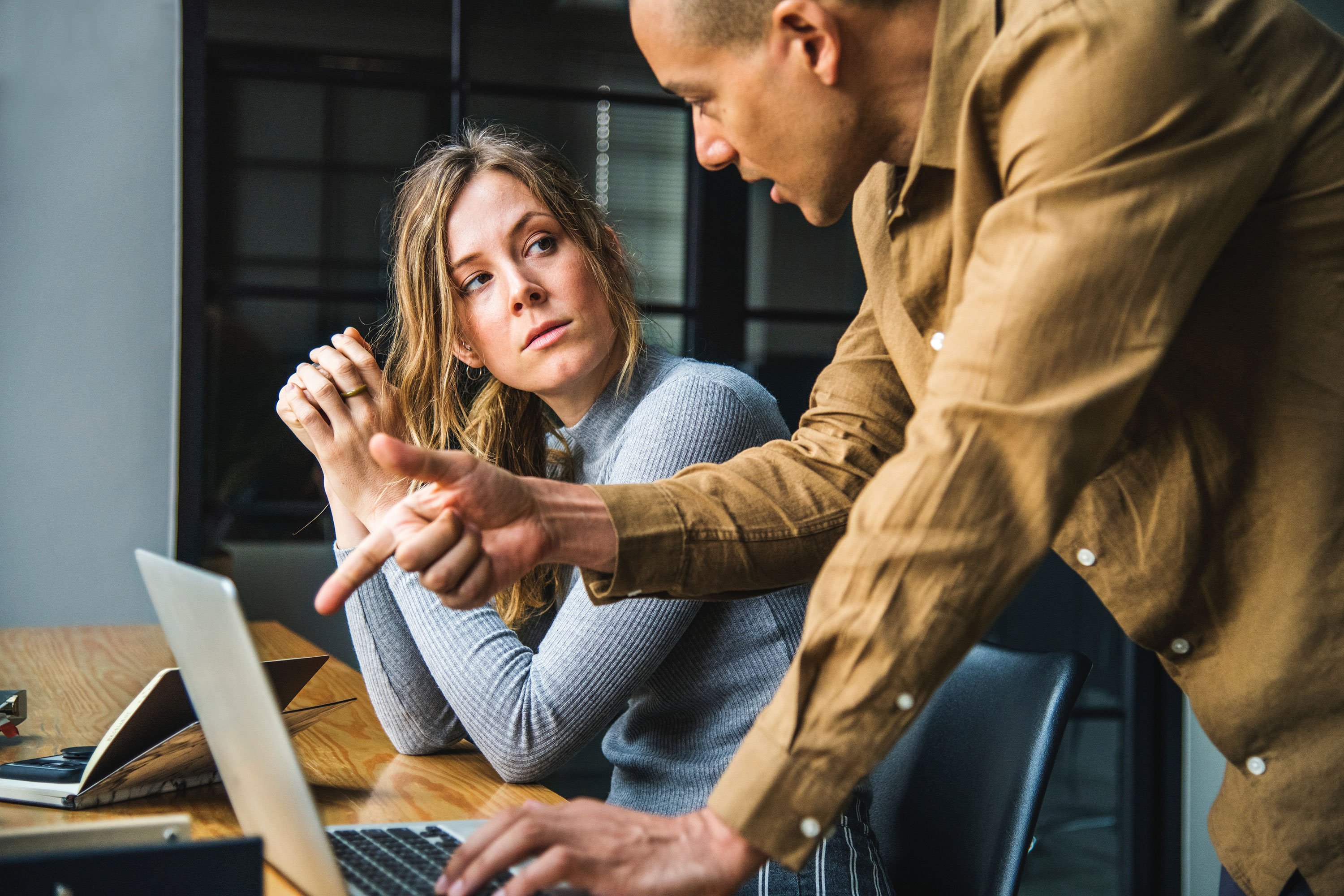 Man and woman working together, man pointing at laptop on desk